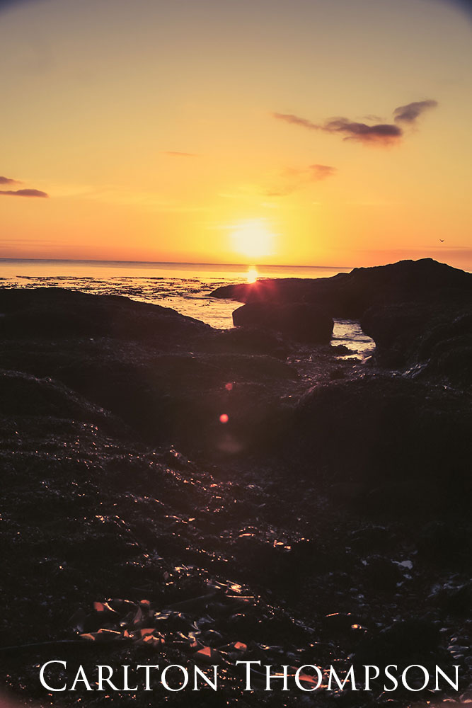 An orange sunrise along a shoreline.