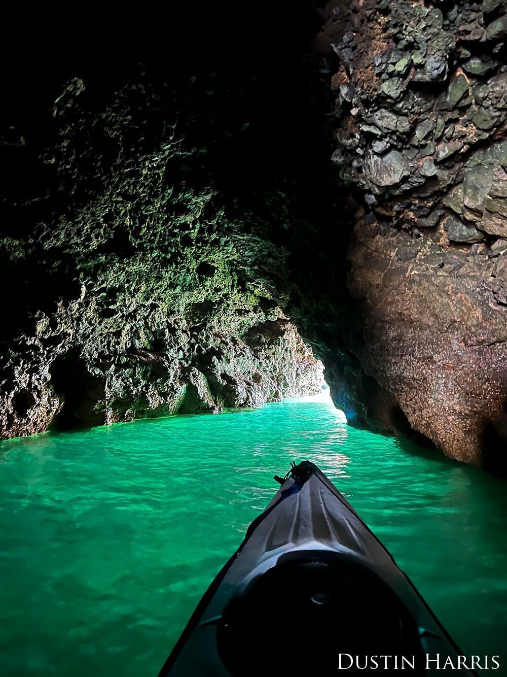POV photo from a kayak in a cave surrounded by green water.