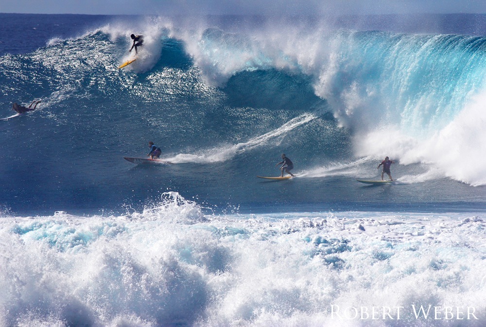 Group of surfers ride large barreling wave.