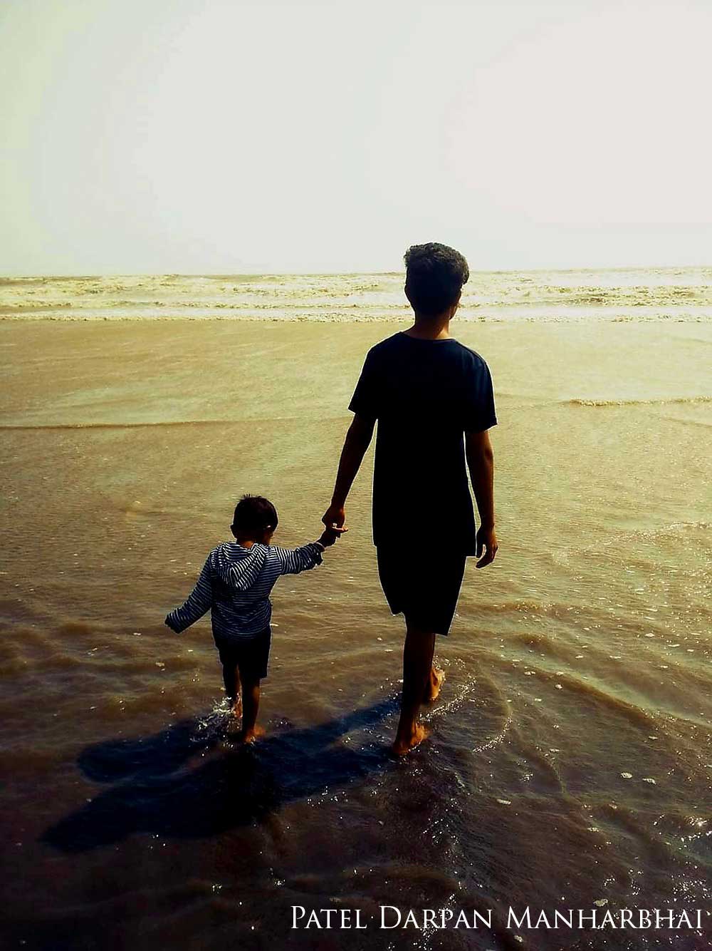 A man and a small boy hold hands while walking on the beach.