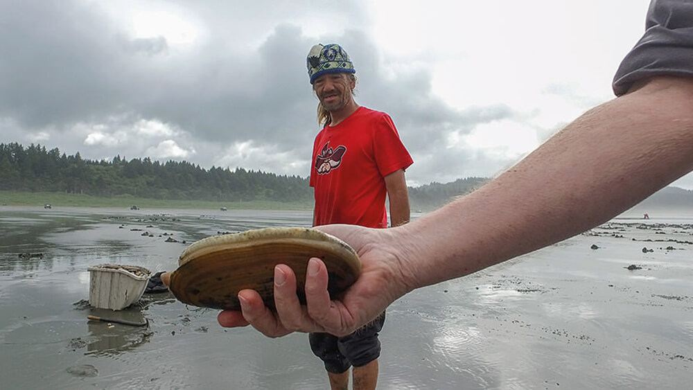 a person holding a large razor clam on a beach