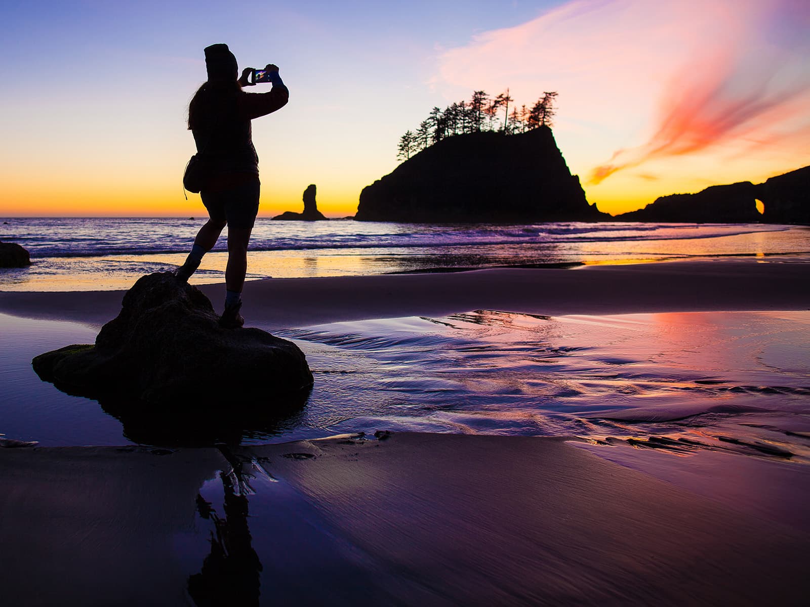A woman photographing the sunset at the beach