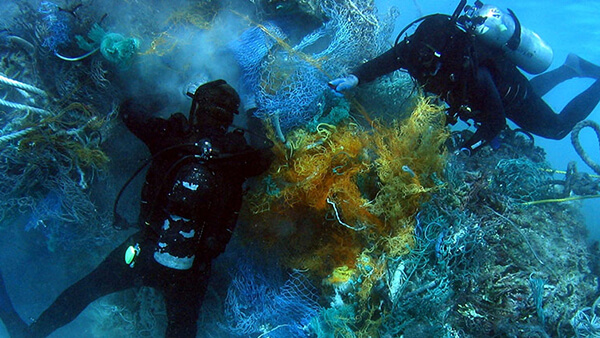 two divers clean marine debris out of a reef