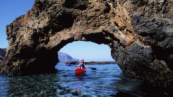 Kayaker paddles through an arch rock formation