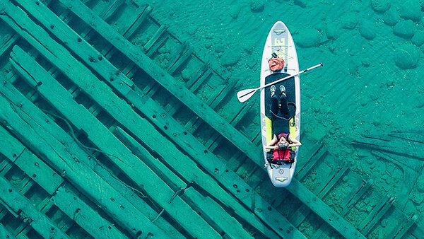 a person lies on a paddleboard while floating above a shipwreck