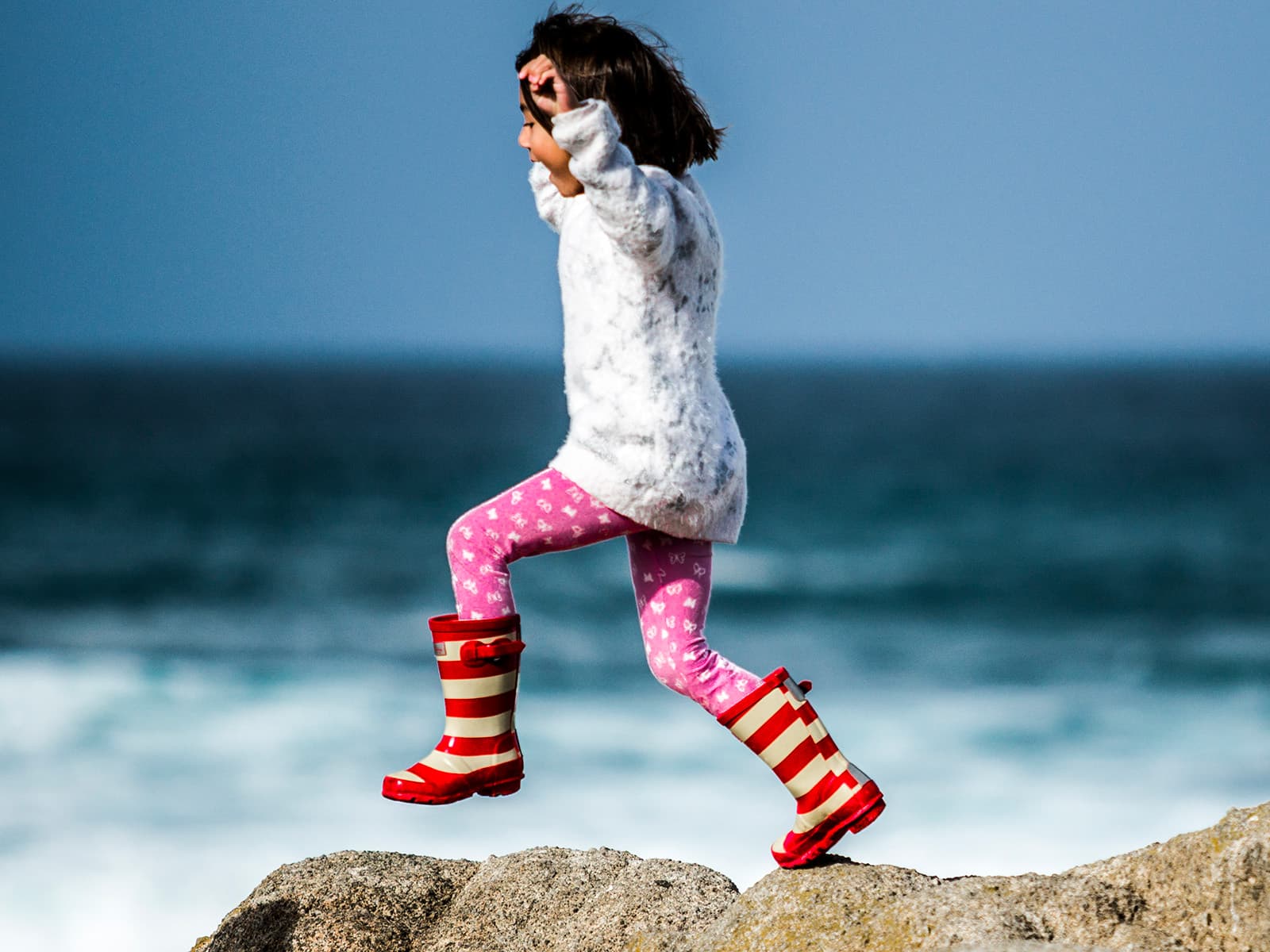 A little girl jumps happily on top of rocks beside the ocean
