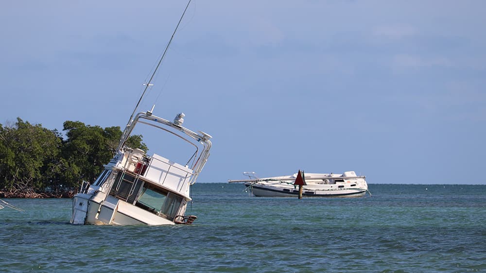 a motor vessel that has run aground and is tilted on its side and taking on water, next to a sailing vesselw ith a collapsed mast that has also run aground