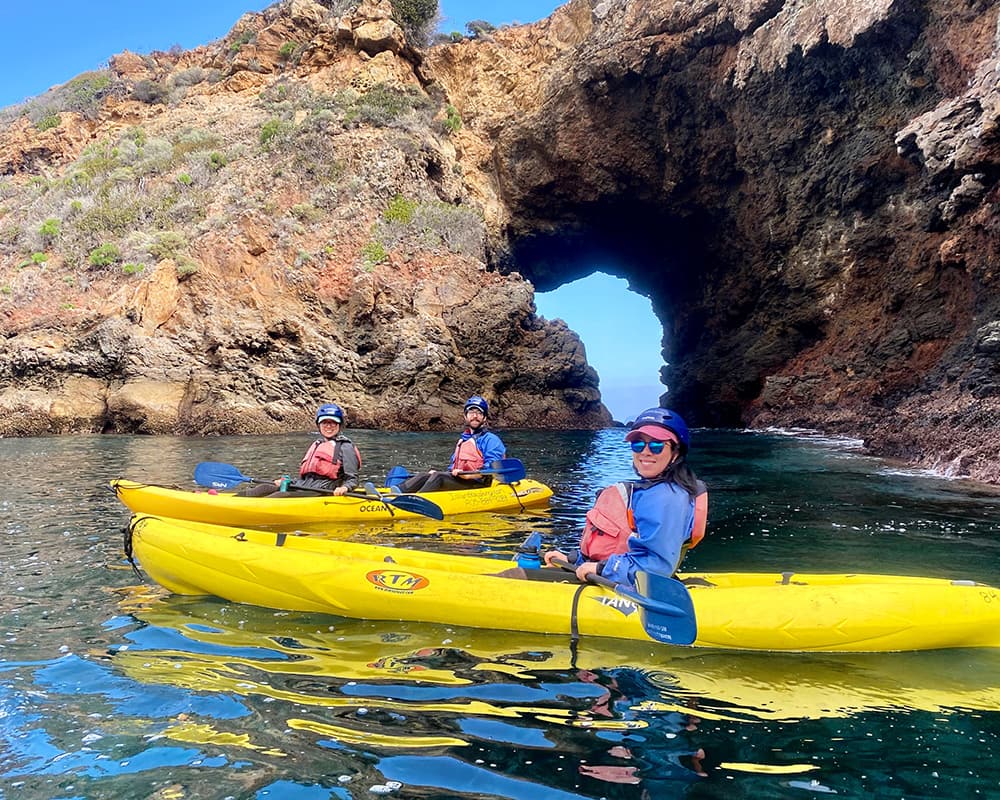 people on kayaks in front of large rocks shaped into an arch