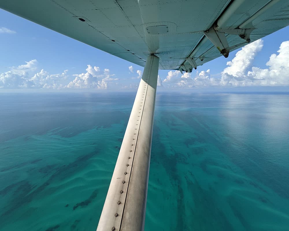 view of tropical blue and turquoise waters from the window seat of an airplane