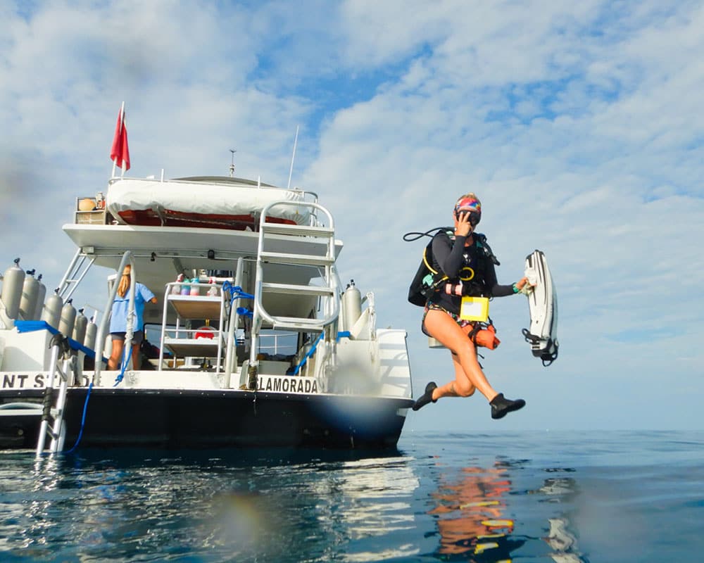 a person takes a giant stride entry into the water from a dive boat while wearing full scuba gear
