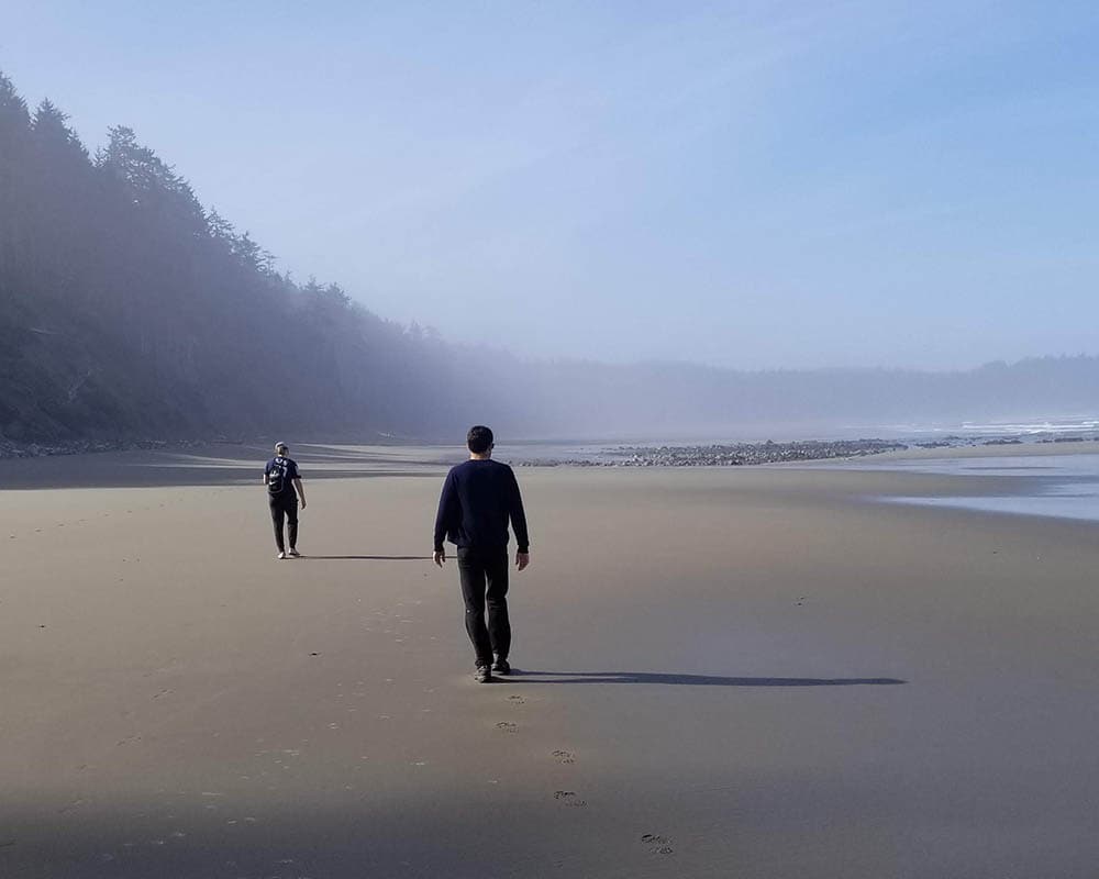 hikers walk along a remote beach on a foggy day with cliffs and rocky outrops in the background