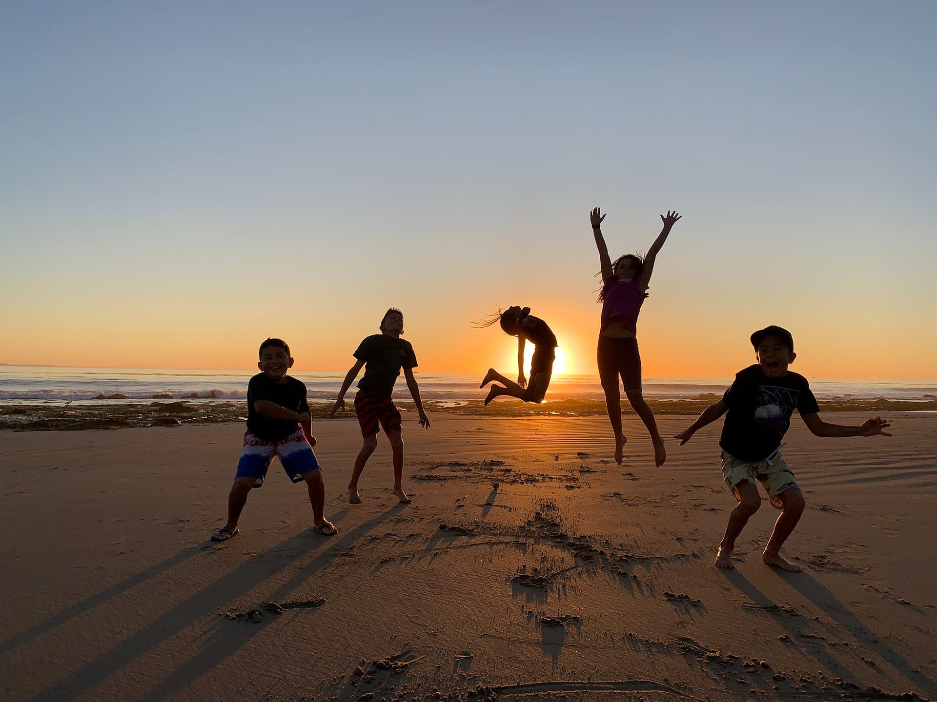 kids jump for joy on a beach with the sunset and ocean in the background