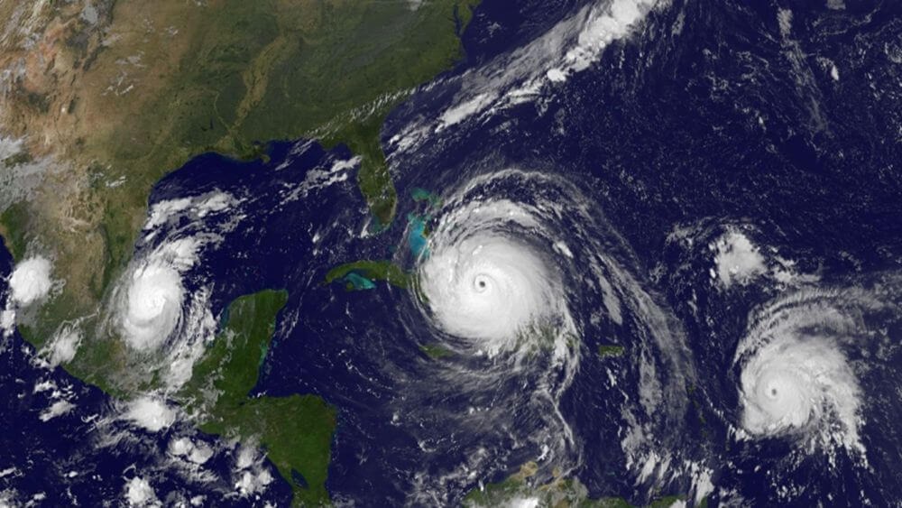 Satellite image of hurricanes in the gulf and atlantic ocean. Land is green and brown with the lower half of the U.S., Mexico, and Caribbean in view.