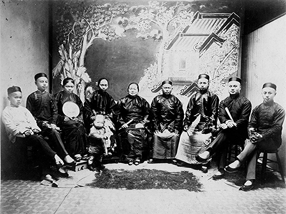 A historic photo shows a family in formal Chinese dress of the early 1900s seated in a circle for a formal portrait.
