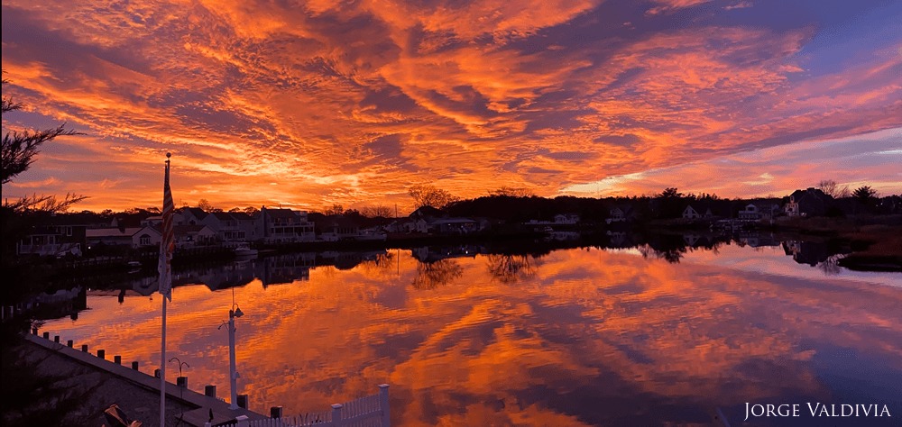 An orange, blue and yellow sunset being reflected against glassy-flat water.