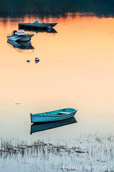 Boats on calm waters at sunset with sunset reflecting into the water.