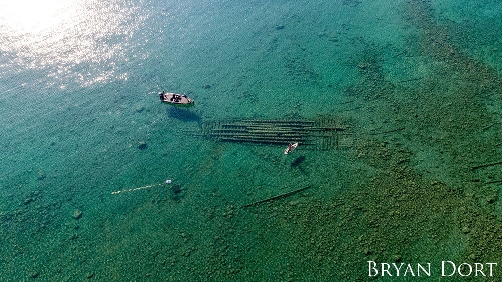 An overview shot of an angler and a paddleboarder with a shipwreck under the crystal clear lake.