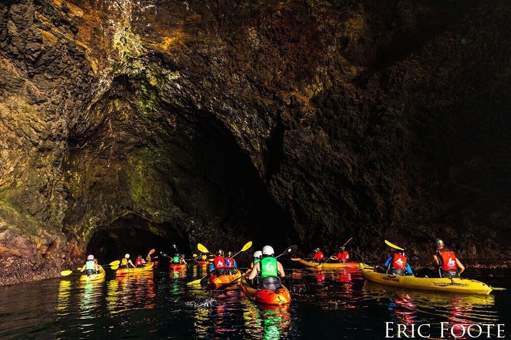A group of kayakers enter a large partially-submerged cave.
