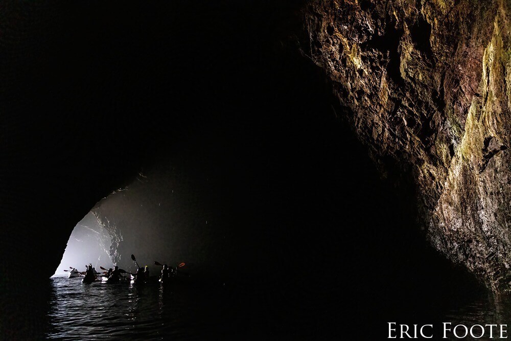 Kayakers paddle towards the light at the mouth of the cave.
