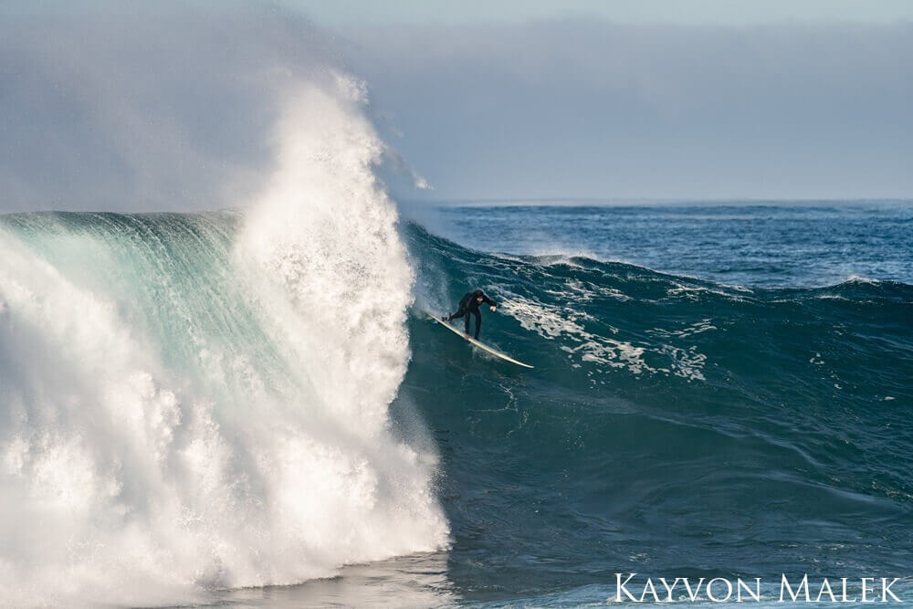 A surfer breaks through a large wave that has begun to spill over and create a tunnel.
