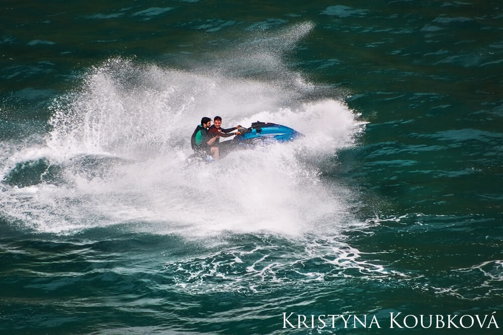 Two people riding a jet ski as it crests over a large wave.
