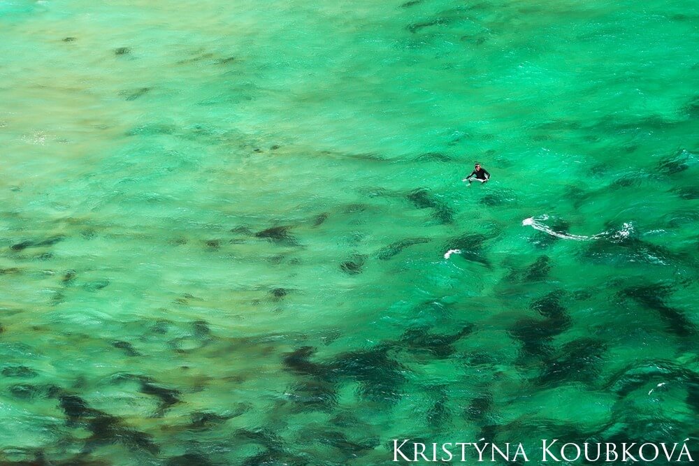 A surfer waits on his surfboard floating on the clear waters.