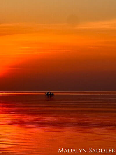 The dark sillouette of a fisherman rigging lines during a golden sunset on the pristine waters of Lake Huron's Thunder Bay National Marine Sanctuary.