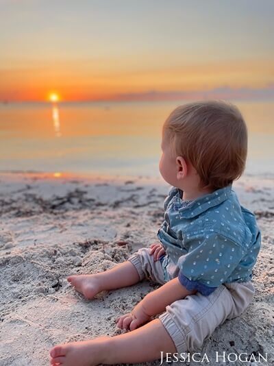 A baby boy views the marvelous sunset from the beach.