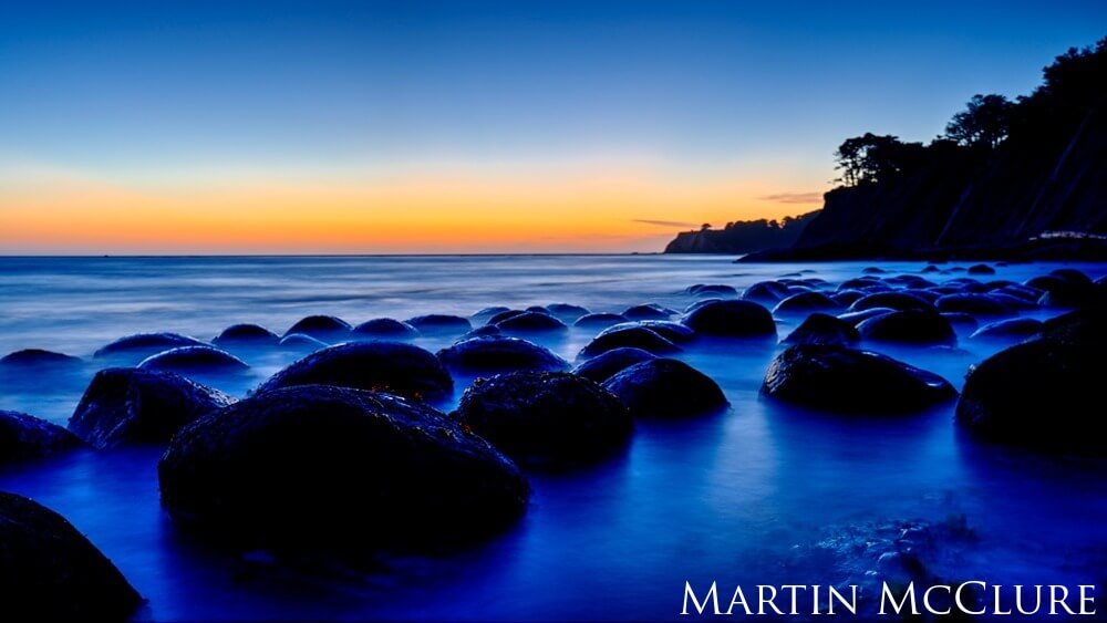 Sun setting over bowling ball looking rocks along the coastline.