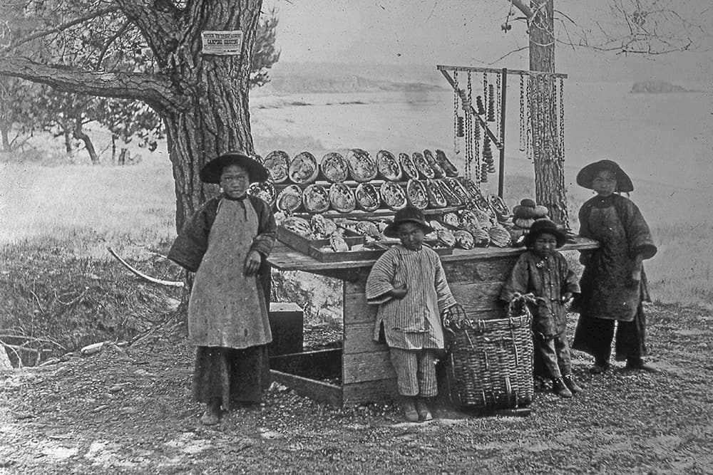 a woman and three children stand in front of a wooden stand holding large abalone shells