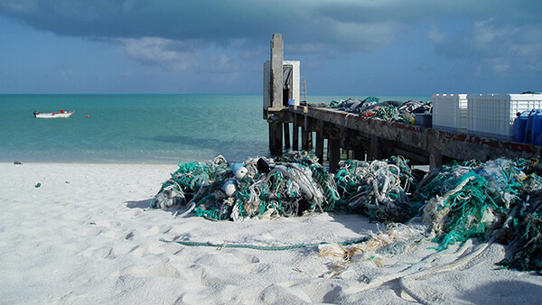 Beach with pier on right hand side with fishing debris and nets on and by the pier.