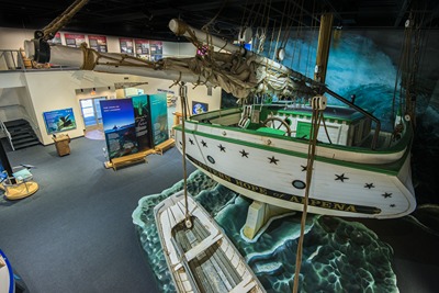 a life-sized replica of a wooden sailboat in a room with exhibit panels and benches