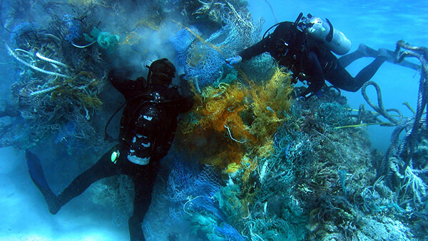 Two divers examine tangled fishing nets on the seafloor
