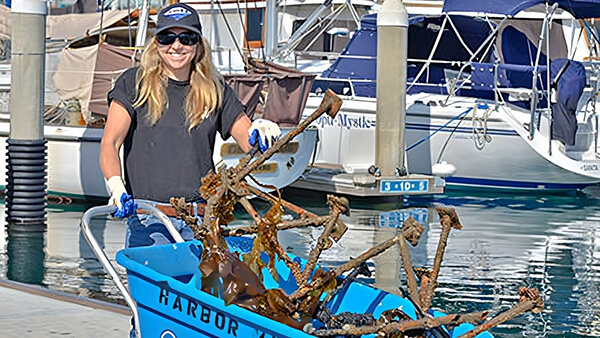 A woman pushes a wheelbarrow containing marine debris
