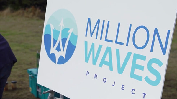 White sign reading “MILLION WAVES PROJECT” in blue writing with logo on left hand side.