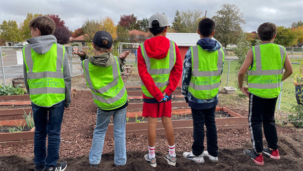 Five students overlooking a school garden wearing green construction style vests with handwritten labels of “Green Team.”