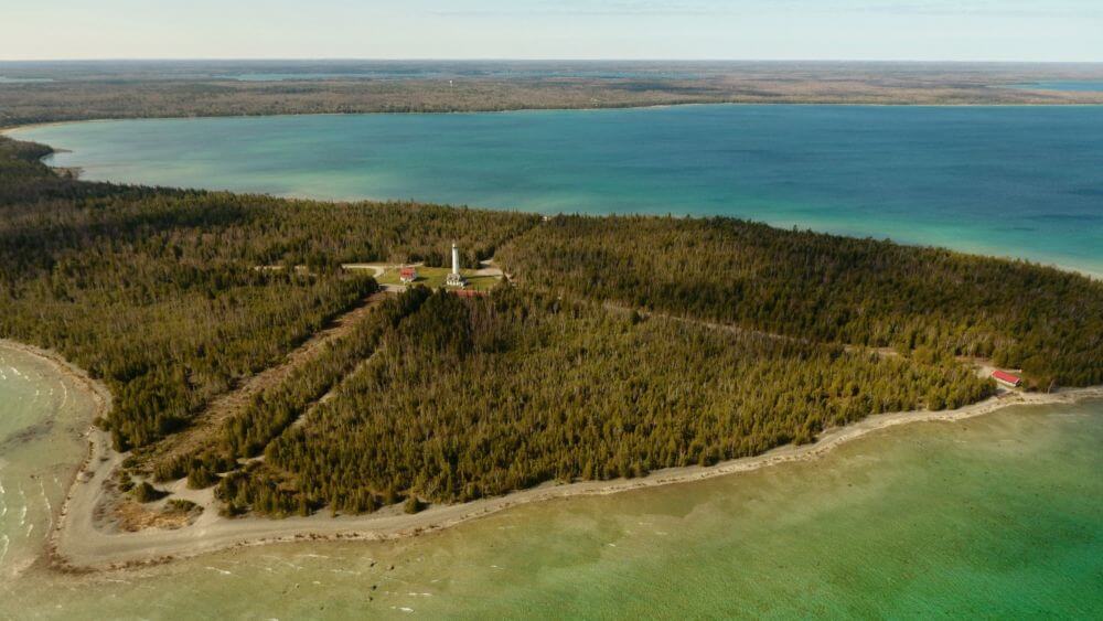 An aerial view of a lighthouse in the forest, on a coast.