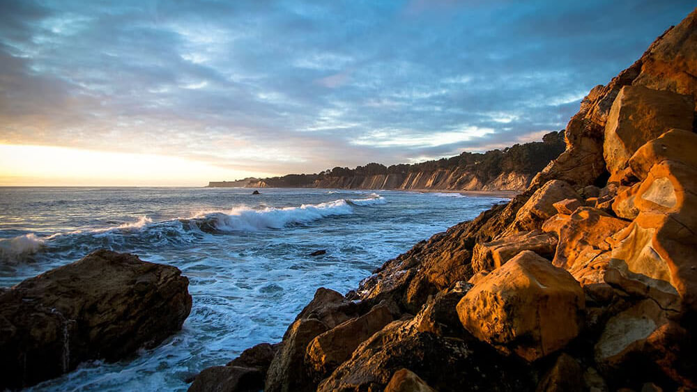 the sun setting on a rocky coastline