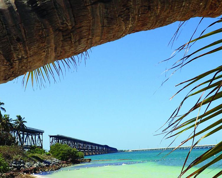 views from a sandy beach showing a railroad bridge passing over tropical turquoise waters