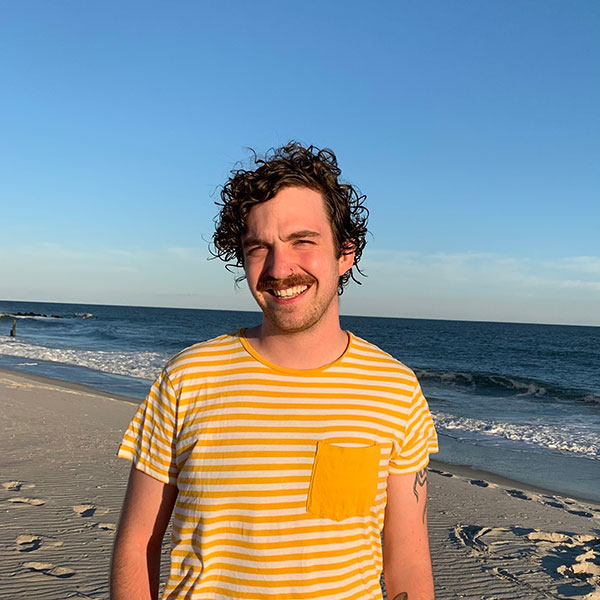 A person smiling on the beach in a yellow striped shirt.