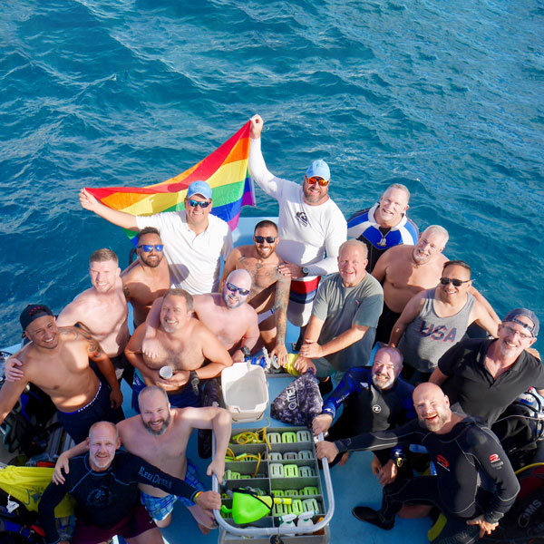 SCUBA divers on a boat pose with a Pride Flag and diving equipment