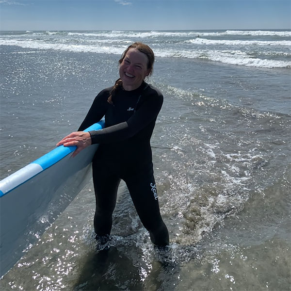 A person smiling on the beach holding a surfboard