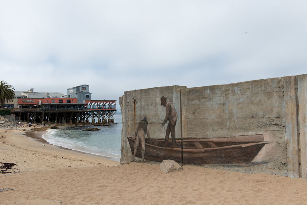 A mural of two historical Chinese fishers is painted on the cement foundation of a ruined building near a beach.