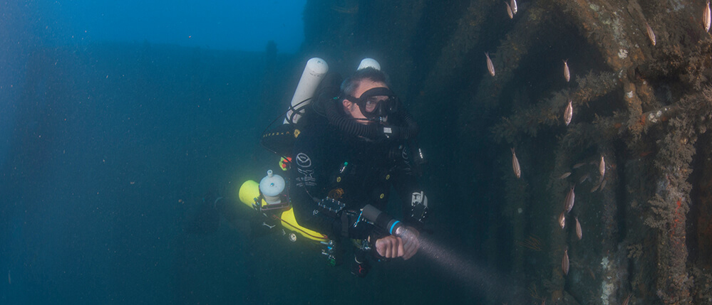 A diver points his flashlight at a shipwreck