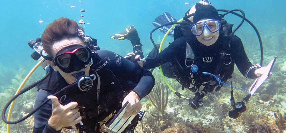 The diver on the left gives a thumbs up while the diver on right smiles