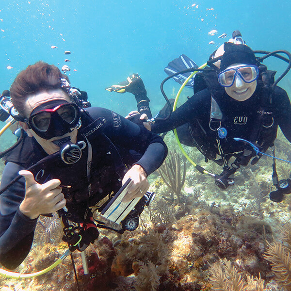 The diver on the left gives a thumbs up while the diver on right smiles