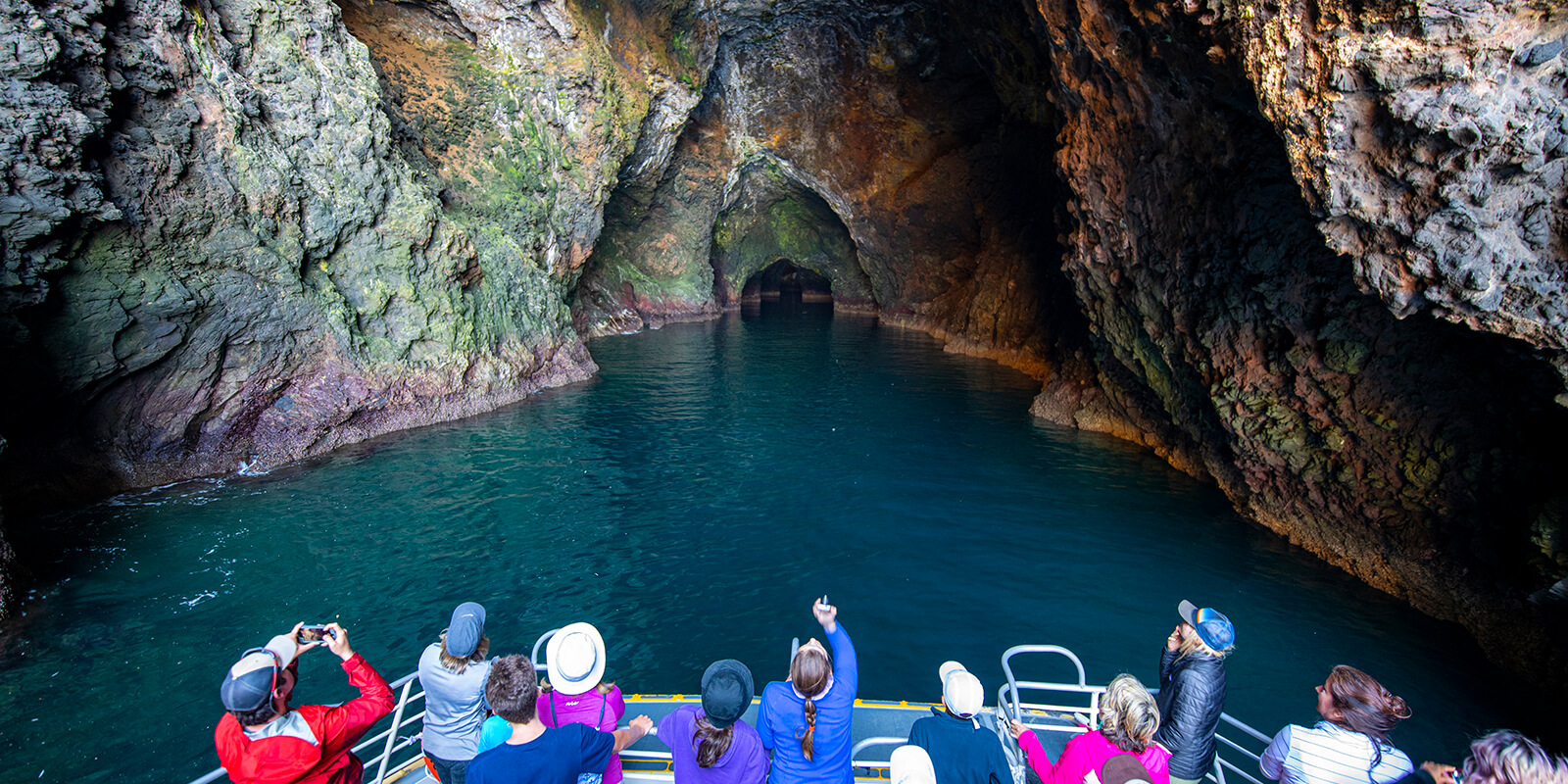 People on a boat take photographs of the entrance to a cave