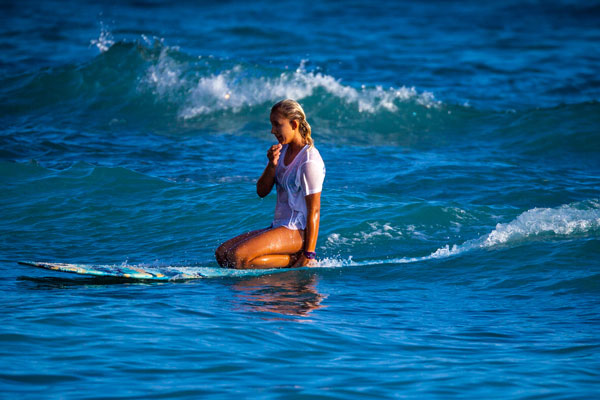 a surfer kneels on her board while she waits for a wave