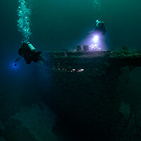 Two divers shine lights on shipwrecks