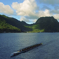 a long boat being rowed with green mountains in the background